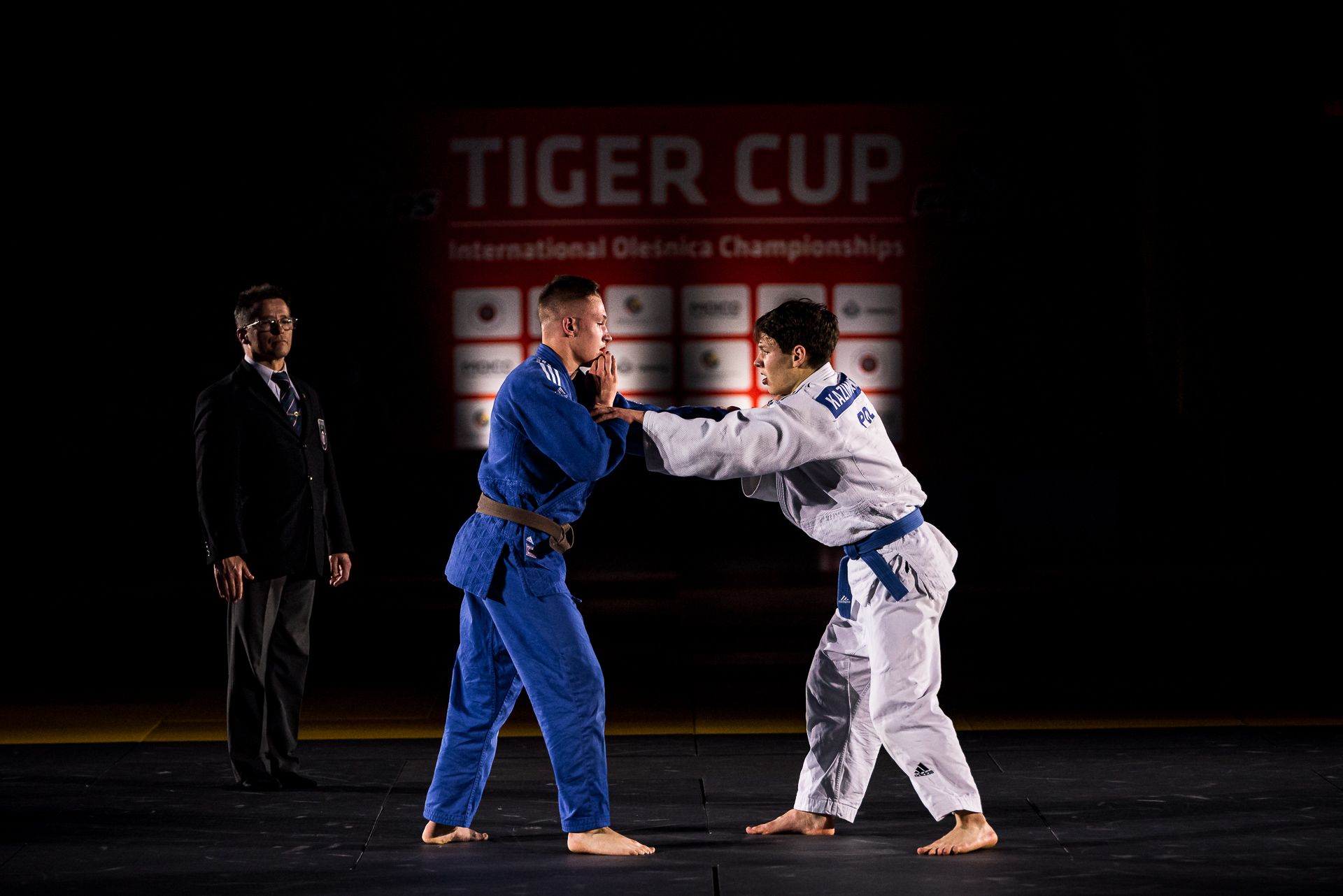 Tiger Cup 2021. Dwóch judoków walczy na gali finałowej zawodów. W tle sędzia i podium.