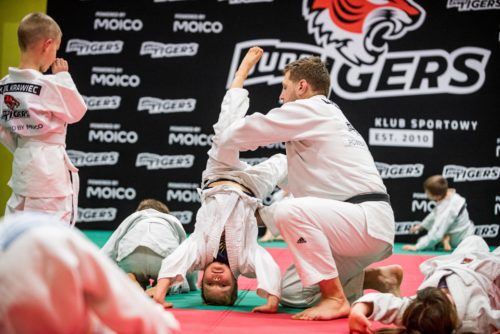 Trener Michał Zamęcki asekuruje chłopca podczas ćwiczeń gimnastycznych na treningu judo (KS Judo Tigers)